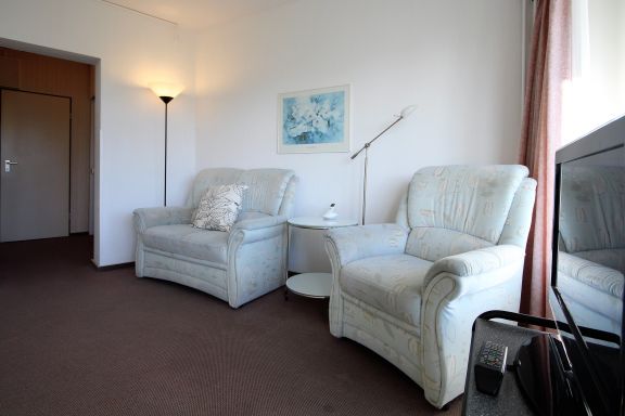 Wohnzimmer mit Sessel, Schrankbett, Küchenzeile und Zugang zur verglasten Loggia