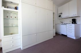 Wohnzimmer mit Sessel, Schrankbett, Küchenzeile und Zugang zur verglasten Loggia